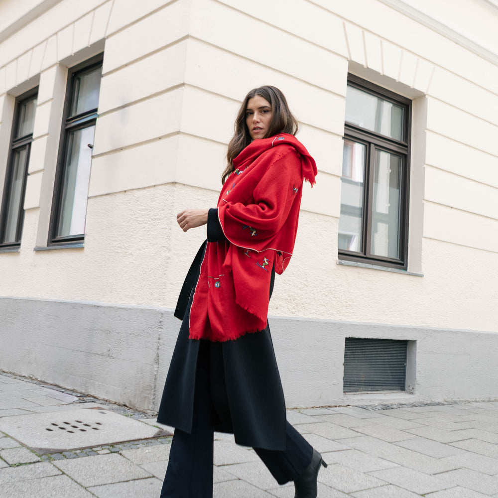 
                      
                        Lifestyle-Aufnahme des handbestickten Pashmina Schals „The Adorned – Alpine Life“; rotes Kaschmir, inspiriert vom alpinen Winterleben und traditioneller Handwerkskunst.
                      
                    