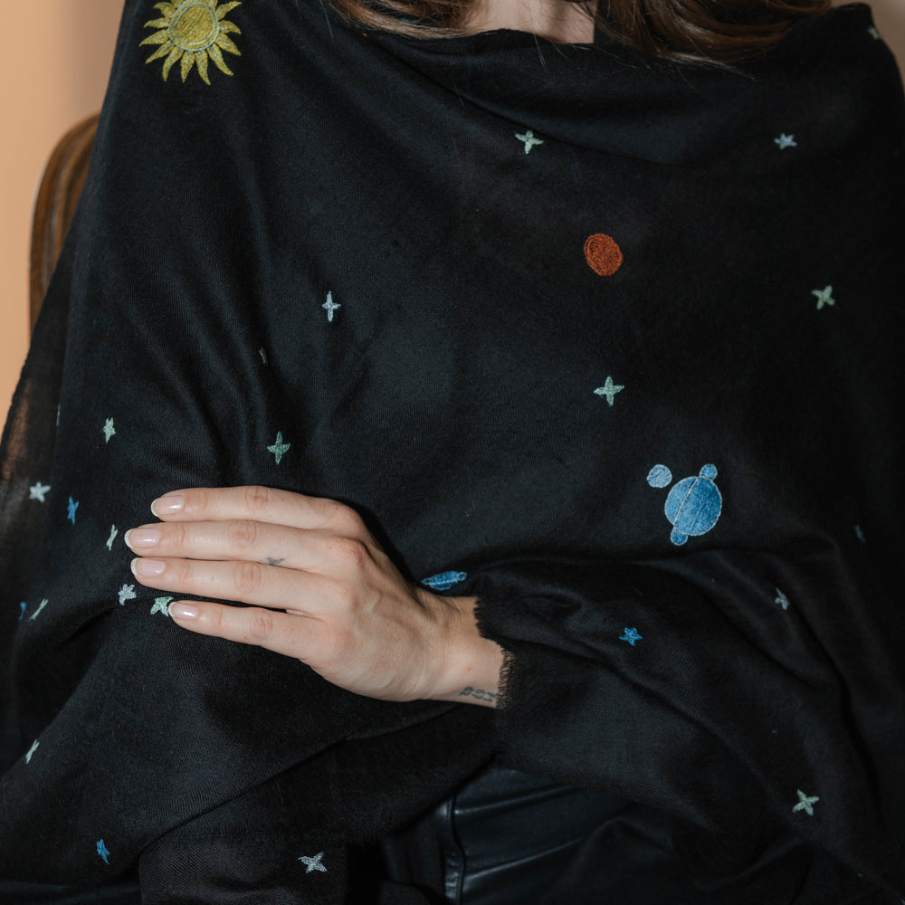 Model trägt den schwarzen Pashmina Schal „The Adorned – Dancing Universe“ mit farbiger Universumsstickerei; handgefertigtes Kaschmir, inspiriert vom mystischen Kosmos.
